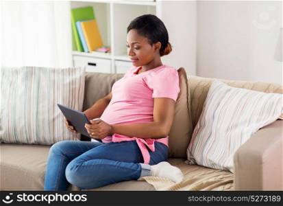 pregnancy, technology and people concept - happy pregnant african american woman with tablet pc computer at home. happy pregnant woman with tablet pc at home