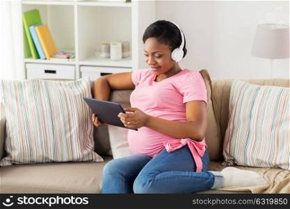 pregnancy, technology and people concept - happy pregnant african american woman with headphones and tablet pc computer at home. pregnant woman in headphones with tablet pc