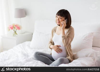 pregnancy, technology and people concept - happy pregnant asian woman calling on smartphone at home. happy pregnant woman calling on smartphone at home