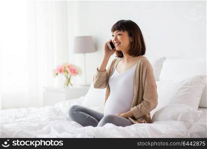 pregnancy, technology and people concept - happy pregnant asian woman calling on smartphone at home. happy pregnant woman calling on smartphone at home