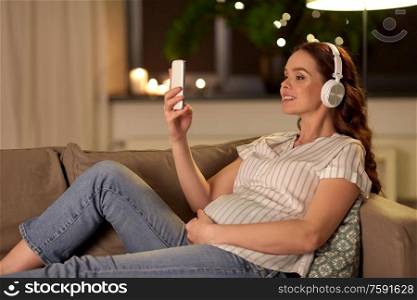 pregnancy, technology and people concept - happy pregnant woman with smartphone and headphones listening to music at home. pregnant woman with smartphone and headphones