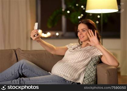 pregnancy, technology and people concept - happy smiling pregnant woman taking selfie with smartphone on sofa at home. happy smiling pregnant woman taking selfie at home