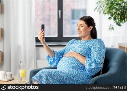 pregnancy, technology and people concept - happy smiling pregnant woman with smartphone at home. happy pregnant woman with smartphone at home