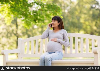 pregnancy, technology, people and communication concept - happy pregnant asian woman calling on smartphone at park. pregnant asian woman calling on smartphone at park