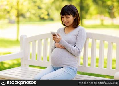 pregnancy, technology, people and communication concept - happy pregnant asian woman with smartphone at park. happy pregnant asian woman with smartphone at park