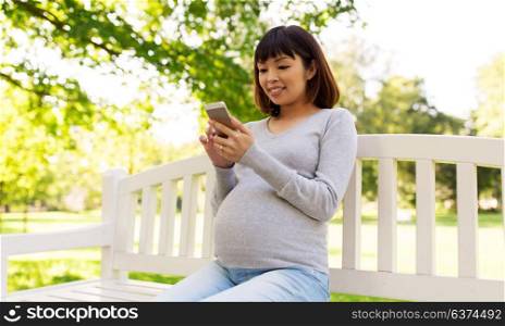 pregnancy, technology, people and communication concept - happy pregnant asian woman with smartphone at park. happy pregnant asian woman with smartphone at park