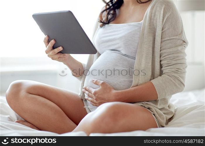 pregnancy, technology, people and expectation concept - close up of pregnant woman with tablet pc computer in bed at home
