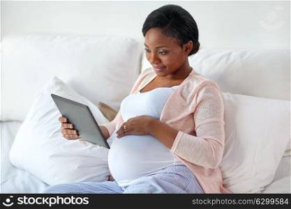 pregnancy, technology, people and expectation concept - happy pregnant african american woman with tablet pc computer in bed at home. happy pregnant woman with tablet pc at home