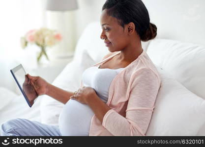 pregnancy, technology, people and expectation concept - happy pregnant african american woman with tablet pc computer in bed at home. happy pregnant woman with tablet pc at home