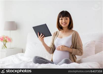 pregnancy, technology, people and expectation concept - happy pregnant asian woman with tablet pc computer in bed at home. happy pregnant asian woman with tablet pc at home