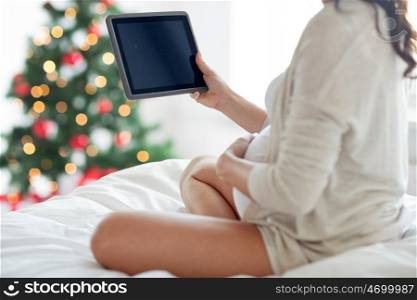 pregnancy, technology, people and holidays concept - close up of pregnant woman with tablet pc computer in bed at home over christmas tree background
