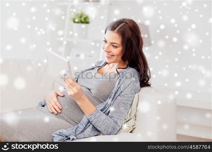 pregnancy, technology, people, christmas and winter concept - happy pregnant woman with tablet pc computer at home over snow