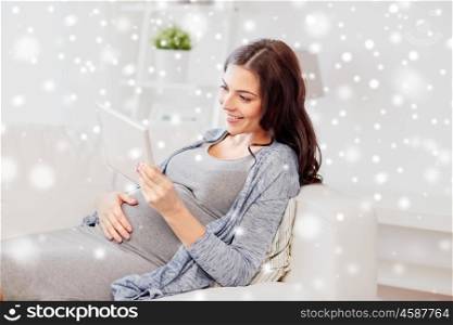 pregnancy, technology, people, christmas and winter concept - happy pregnant woman with tablet pc computer at home over snow