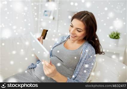 pregnancy, technology, winter, christmas and people concept - happy pregnant woman with tablet pc computer and credit card shopping online at home over snow