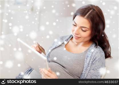 pregnancy, technology, winter, christmas and people concept - happy pregnant woman with tablet pc computer and credit card shopping online at home over snow