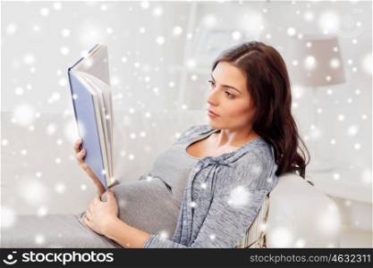 pregnancy, winter and motherhood concept - pregnant woman lying on sofa and reading book over snow
