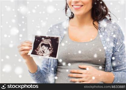 pregnancy, winter and people concept - close up of happy pregnant woman holding at ultrasound image at home over snow