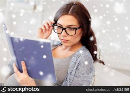 pregnancy, winter, christmas and motherhood concept - pregnant woman lying on sofa and reading book over snow