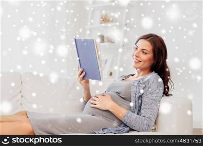 pregnancy, winter, christmas and motherhood concept - smiling pregnant woman lying on sofa and reading book over snow