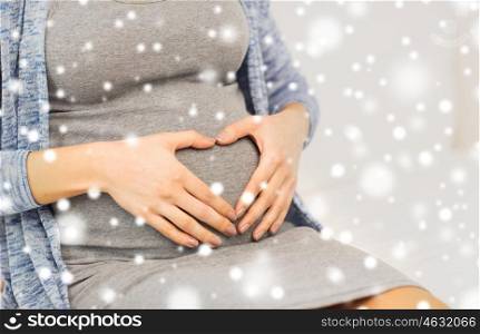 pregnancy, winter, christmas, people and expectation concept - close up of pregnant woman belly and heart shape over snow