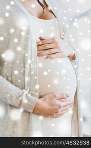 pregnancy, winter, christmas, people and expectation concept - close up of pregnant woman belly and hands over snow