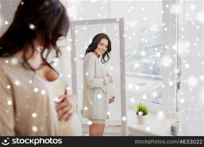 pregnancy, winter, christmas, people and expectation concept - happy pregnant woman looking to mirror at home over snow