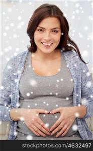 pregnancy, winter, christmas, people and expectation concept - happy pregnant woman making heart gesture at home over snow