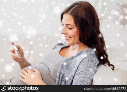 pregnancy, winter, christmas, technology and people concept - happy pregnant woman with smartphone at home over snow