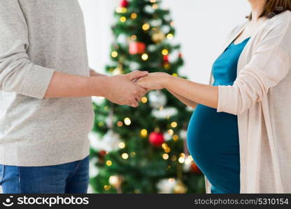 pregnancy, winter holidays and people concept - close up of happy couple holding hands at christmas. close up of man and pregnant woman at christmas