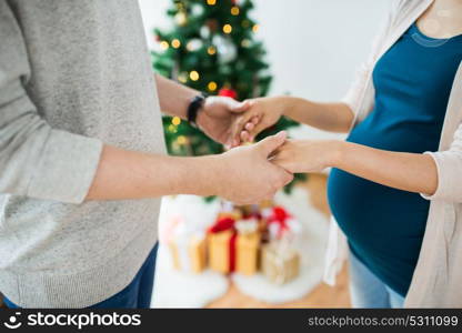 pregnancy, winter holidays and people concept - close up of happy couple holding hands at christmas. close up of man and pregnant woman at christmas