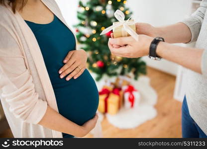 pregnancy, winter holidays and people concept - close up of husband giving christmas present to his pregnant wife at home. husband giving christmas present to pregnant wife