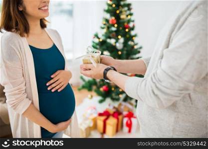 pregnancy, winter holidays and people concept - close up of husband giving christmas present to his pregnant wife at home. husband giving christmas present to pregnant wife