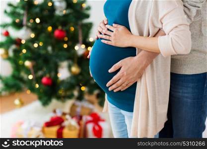 pregnancy, winter holidays and people concept - close up of man touching his pregnant wife belly home at christmas. man and pregnant woman home at christmas
