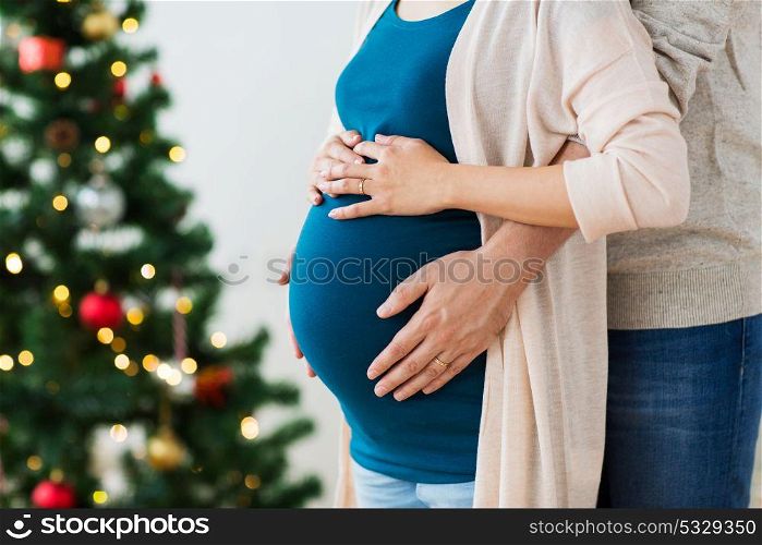 pregnancy, winter holidays and people concept - close up of man touching his pregnant wife belly home at christmas. man and pregnant woman home at christmas