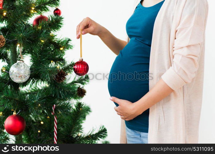 pregnancy, winter holidays and people concept - close up of pregnant woman decorating christmas tree at home. pregnant woman decorating christmas tree