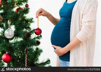pregnancy, winter holidays and people concept - close up of pregnant woman decorating christmas tree at home. pregnant woman decorating christmas tree