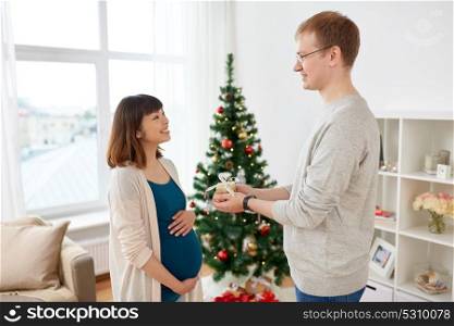 pregnancy, winter holidays and people concept - happy husband giving christmas present to his pregnant wife at home. husband giving christmas present to pregnant wife