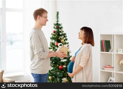 pregnancy, winter holidays and people concept - happy husband giving christmas present to his pregnant wife at home. husband giving christmas present to pregnant wife