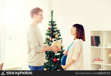 pregnancy, winter holidays and people concept - happy husband giving christmas present to his pregnant wife at home. husband giving christmas present to pregnant wife