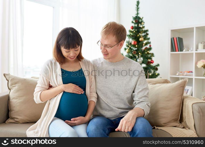 pregnancy, winter holidays and people concept - happy pregnant wife with husband at home at christmas. pregnant wife with husband at home at christmas