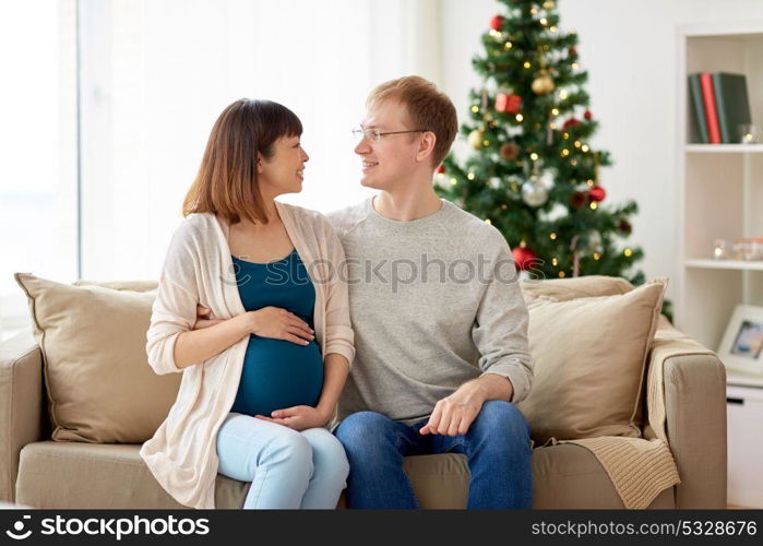 pregnancy, winter holidays and people concept - happy pregnant wife with husband at home at christmas. pregnant wife with husband at home at christmas