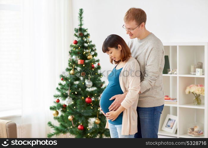 pregnancy, winter holidays and people concept - happy pregnant wife with husband at home at christmas. pregnant wife with husband at home at christmas