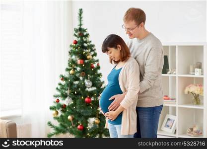 pregnancy, winter holidays and people concept - happy pregnant wife with husband at home at christmas. pregnant wife with husband at home at christmas