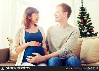 pregnancy, winter holidays and people concept - happy pregnant wife with husband at home at christmas. pregnant wife with husband at home at christmas