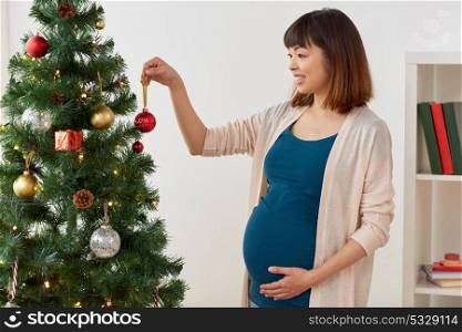 pregnancy, winter holidays and people concept - pregnant asian woman decorating christmas tree at home. pregnant woman decorating christmas tree at home
