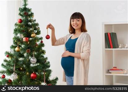 pregnancy, winter holidays and people concept - pregnant asian woman decorating christmas tree at home. pregnant woman decorating christmas tree at home