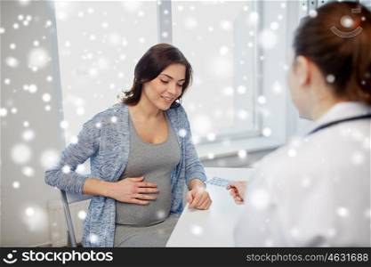 pregnancy, winter, medicine, healthcare and people concept - smiling gynecologist doctor giving pills to pregnant woman meeting at hospital over snow