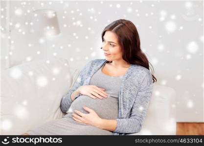 pregnancy, winter, people and expectation concept - happy pregnant woman lying on sofa at home over snow