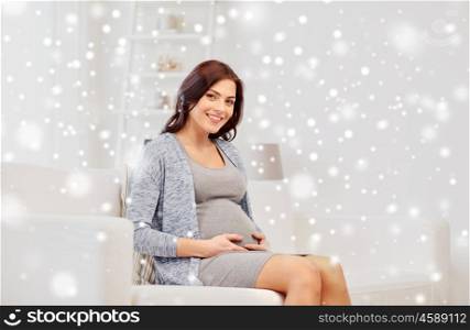 pregnancy, winter, people and expectation concept - happy pregnant woman sitting on sofa at home over snow