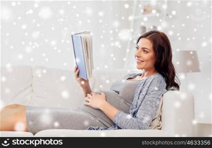 pregnancy, winter, people and motherhood concept - smiling pregnant woman lying on sofa and reading book over snow